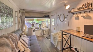 Une pièce confortable avec un canapé, un bureau avec un ordinateur portable, une fenêtre avec des rideaux et une étagère avec des tasses et un calendrier.