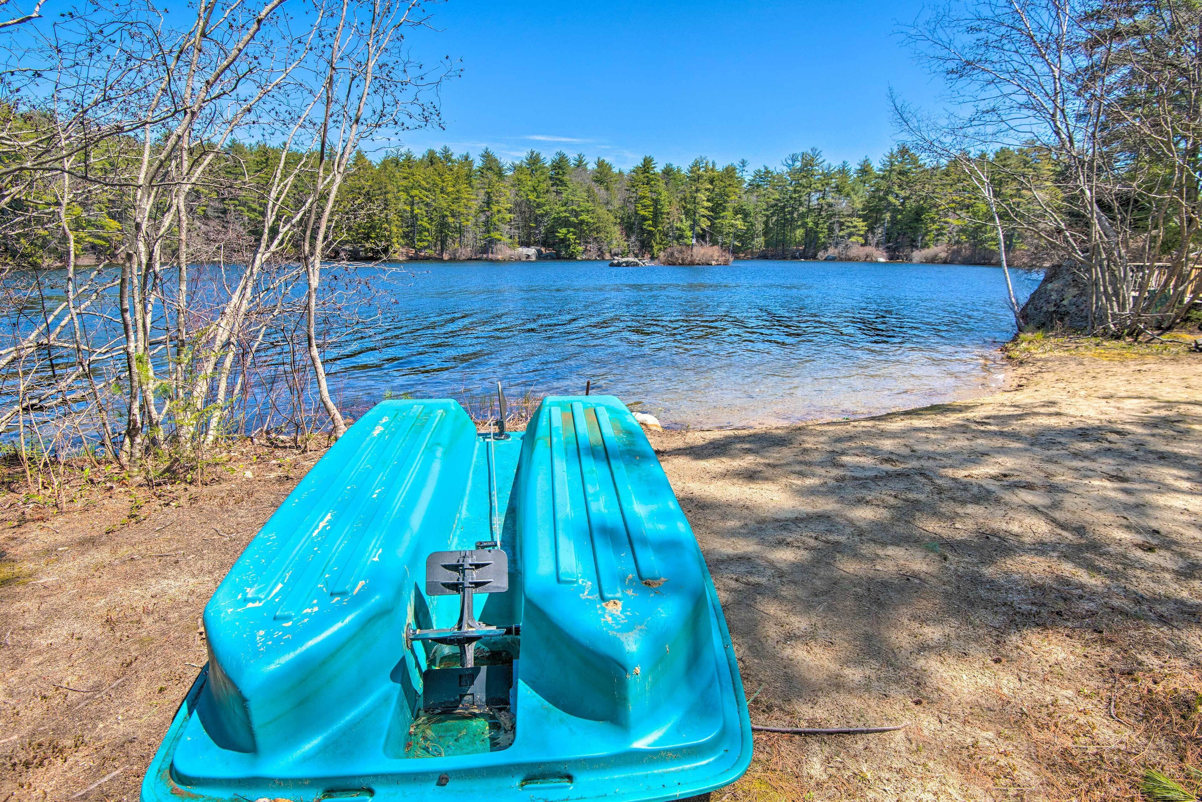 A kayak on a sandy shore with a lake and trees in the background.