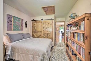 A bedroom with a bed, a wooden wardrobe, a bookshelf, and a painting on the wall. - Hugo Home, Direct Lake Access & Private Dock! (Hugo)
