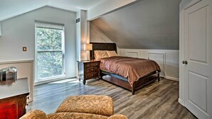 Une chambre avec un plafond en pente, une grande fenêtre, un lit, une table de chevet et une armoire.