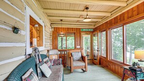 Ein gemütliches Blockhaus-Interieur mit einer Holzwand, einer Couch mit gemusterten Kissen, einem Sessel und einem Tisch mit Büchern und einer Lampe.