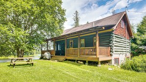 Eine Blockhütte mit Veranda, einem Picknicktisch und einem kleinen Teich im Hintergrund.