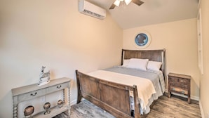 Un dormitorio con cama de madera, ventilador de techo, equipo de aire acondicionado, mesita de noche pequeña y una figurita decorativa de cebra.