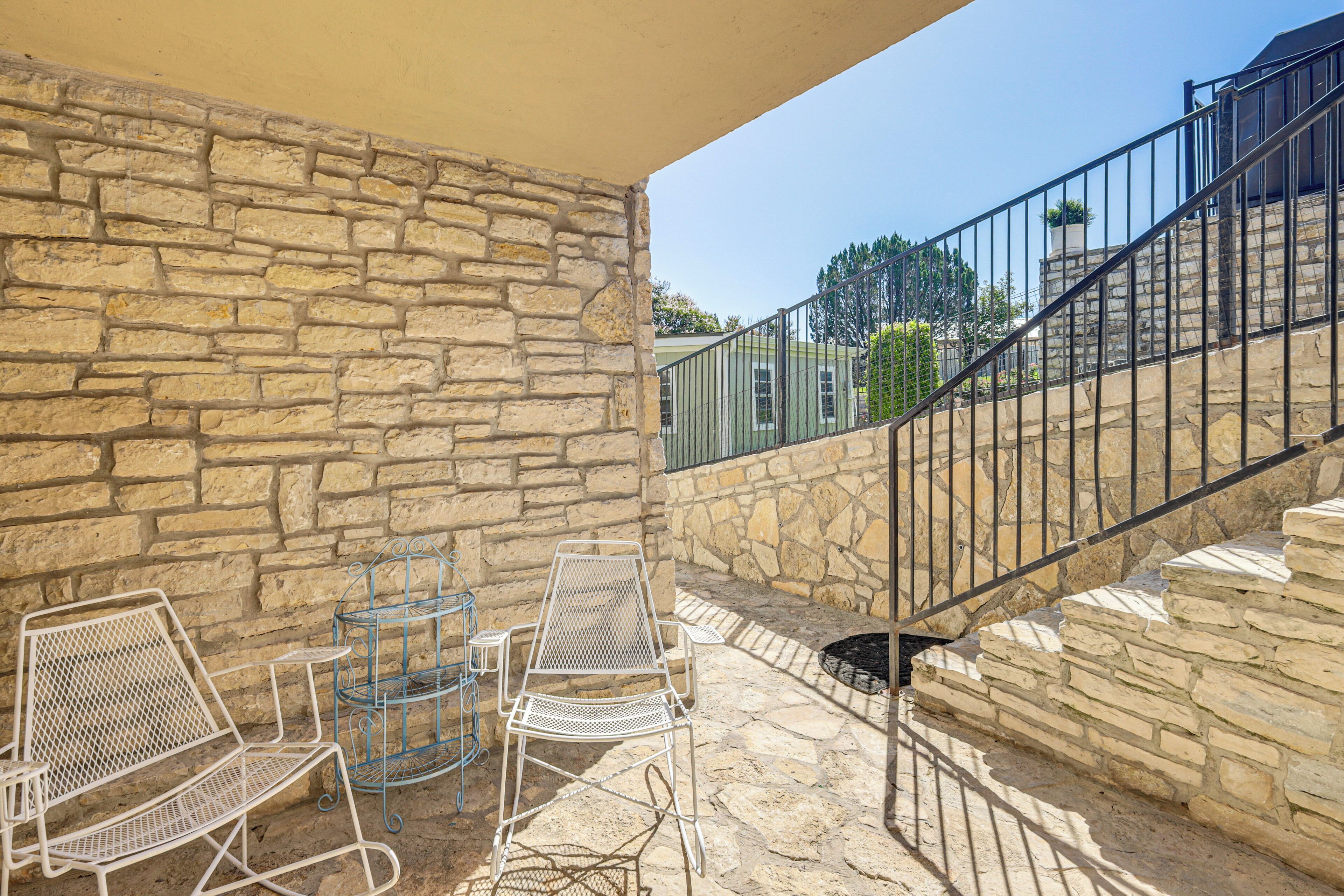 A stone wall with a metal staircase and outdoor seating area with metal chairs and a table.