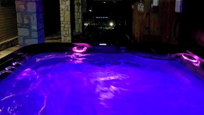 Un bain à remous doté d’un éclairage violet, entouré de murs en pierre et présentant un intérieur sombre.