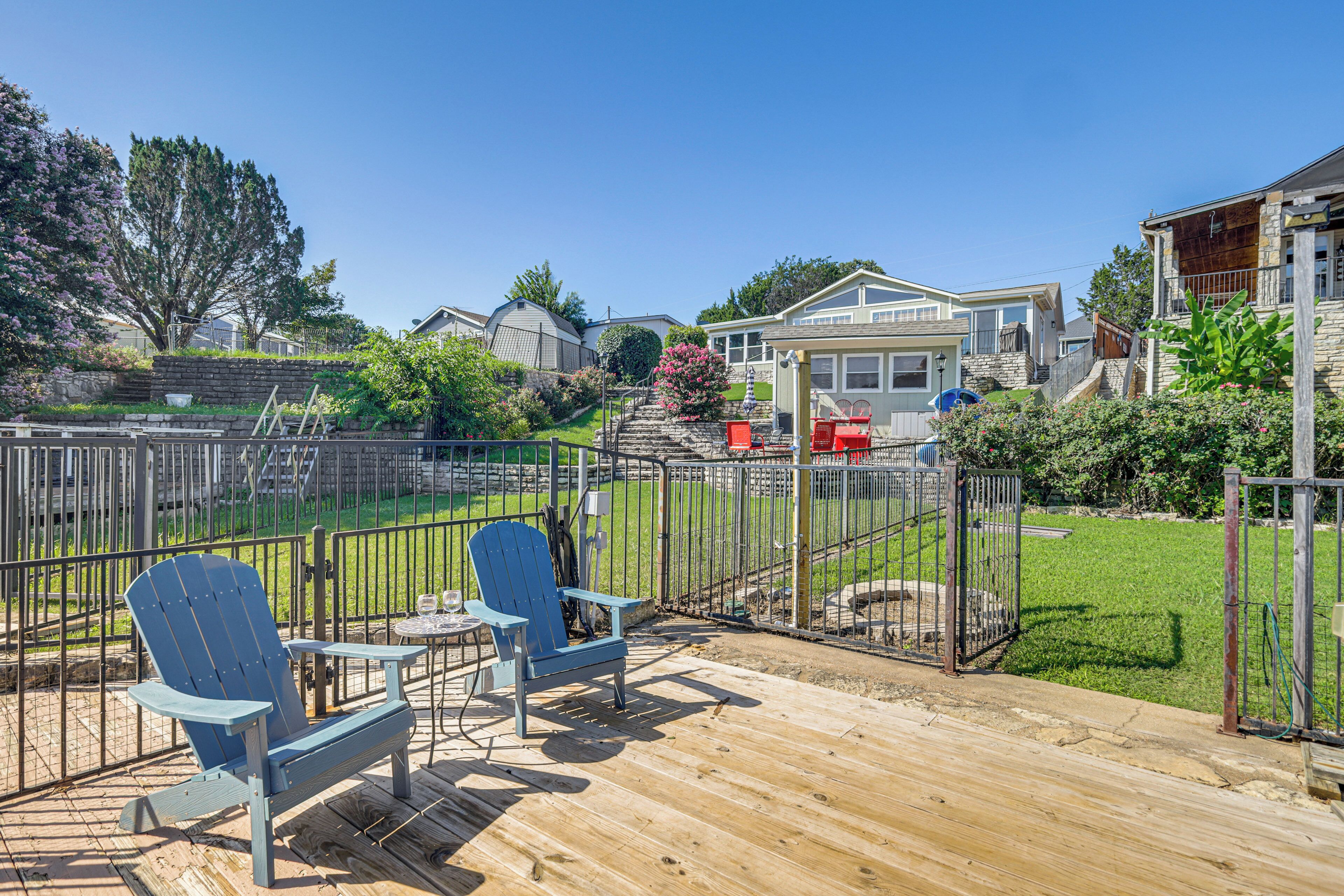 Une terrasse en bois avec deux chaises Adirondack bleues, une petite table et une vue sur un quartier résidentiel avec des maisons et une cour clôturée.