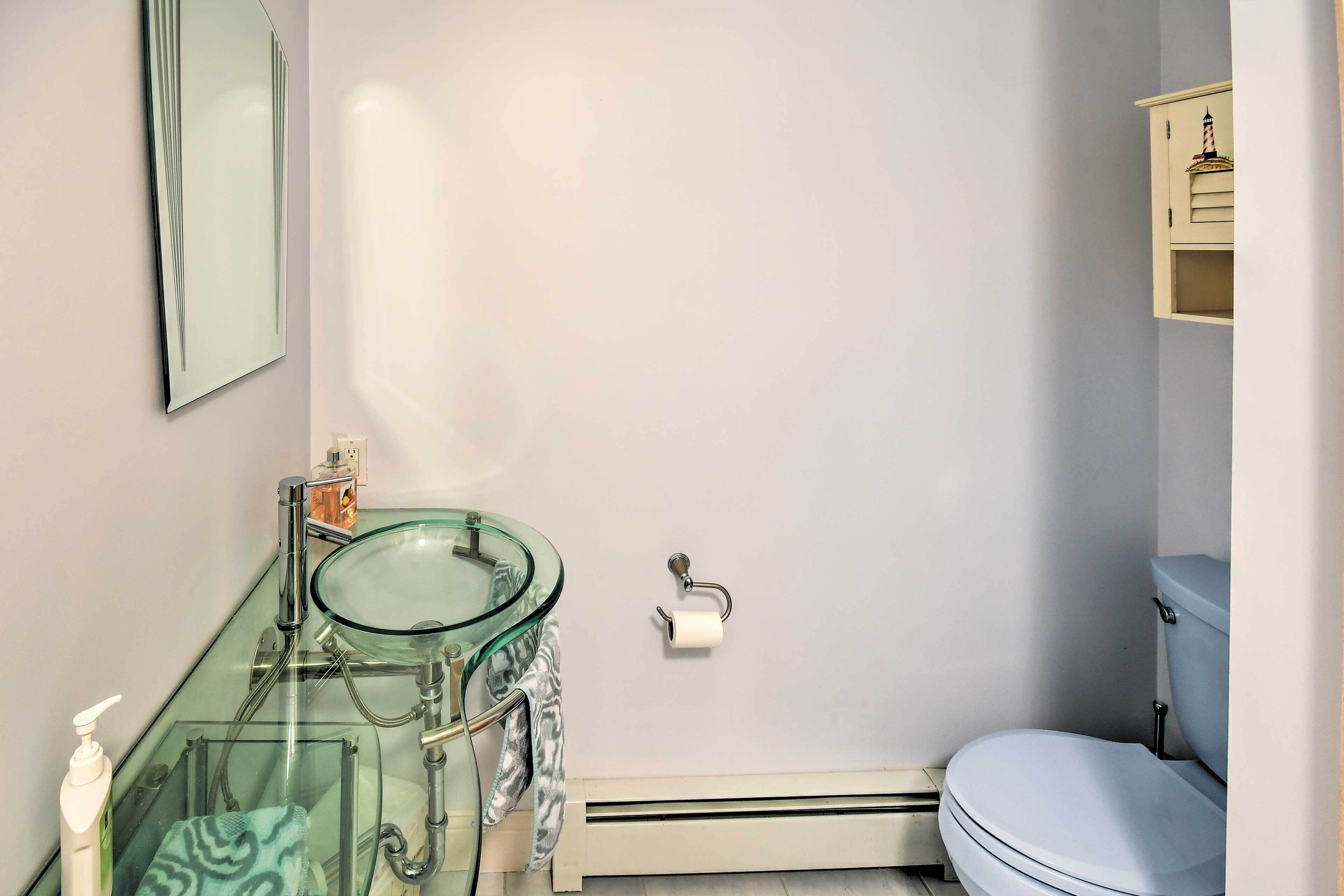A bathroom with a glass sink, toilet, and a small cabinet with a lighthouse decoration.