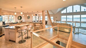 A spacious kitchen with a central island, bar stools, and a view of the water through large windows. - Luxe Oceanfront Home w/ Cadillac Mountain Views! (Sullivan)