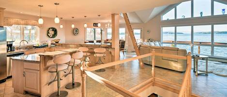 A spacious kitchen with a central island, bar stools, and a view of the water through large windows.
