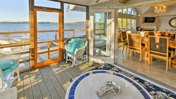 A spacious deck with a view of the water, a dining area with chairs and a table, and a large window. - Luxe Oceanfront Home w/ Cadillac Mountain Views! (Sullivan)