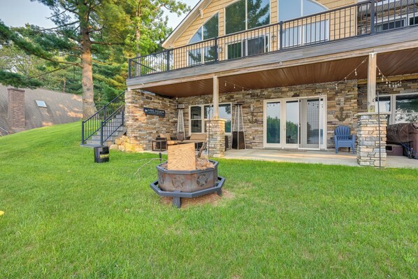 A two-story house with a stone facade, a covered porch, and a fire pit in the yard. - Luxe Waterfront Home w/ Private Lake Access! (West Branch)