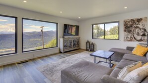 A spacious living room with large windows, a gray sofa, a coffee table, and a cabinet with a flat-screen TV. - Mt Hood Views: Modern Underwood Home w/ Deck! (Underwood)