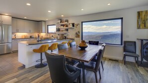A modern kitchen with a large island, dining area with chairs, and a view through a large window. - Mt Hood Views: Modern Underwood Home w/ Deck! (Underwood)