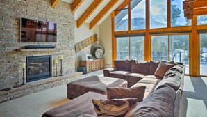 A cozy living room with a stone fireplace, a large window, and a wooden ceiling.