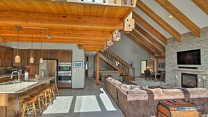 A spacious living area with a high ceiling, wooden beams, a stone fireplace, and a large TV.