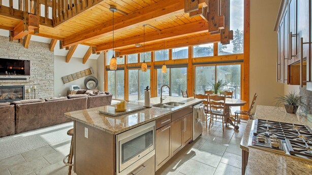 A spacious kitchen with a large island, wooden ceiling beams, and large windows offering views of the outdoors.