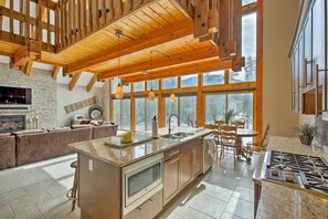 Une cuisine spacieuse dotée d’un grand îlot central, de poutres apparentes en bois au plafond et de grandes fenêtres offrant une vue sur l’extérieur.