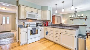 A kitchen with white cabinets, a microwave, a stove, and a sink. There are hanging lights and a shelf above the counter. - Mount Holly Vacation Rental w/ Hot Tub! (Mount Holly)