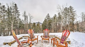 Four wooden Adirondack chairs with skis leaning against them, set on a snow-covered ground with trees in the background. - Mount Holly Vacation Rental w/ Hot Tub! (Mount Holly)