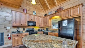 Una cocina con armarios de madera, encimeras de granito, un refrigerador negro y una cafetera.