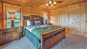 Un dormitorio de cabaña de madera con cama, mesitas de noche, ventilador de techo y un ventanal grande.