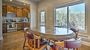 A kitchen with wooden cabinets, a large round table, and chairs. There are windows with a view of trees. - Mammoth Creek Apt. Between Bryce Canyon & Zion! (Hatch)