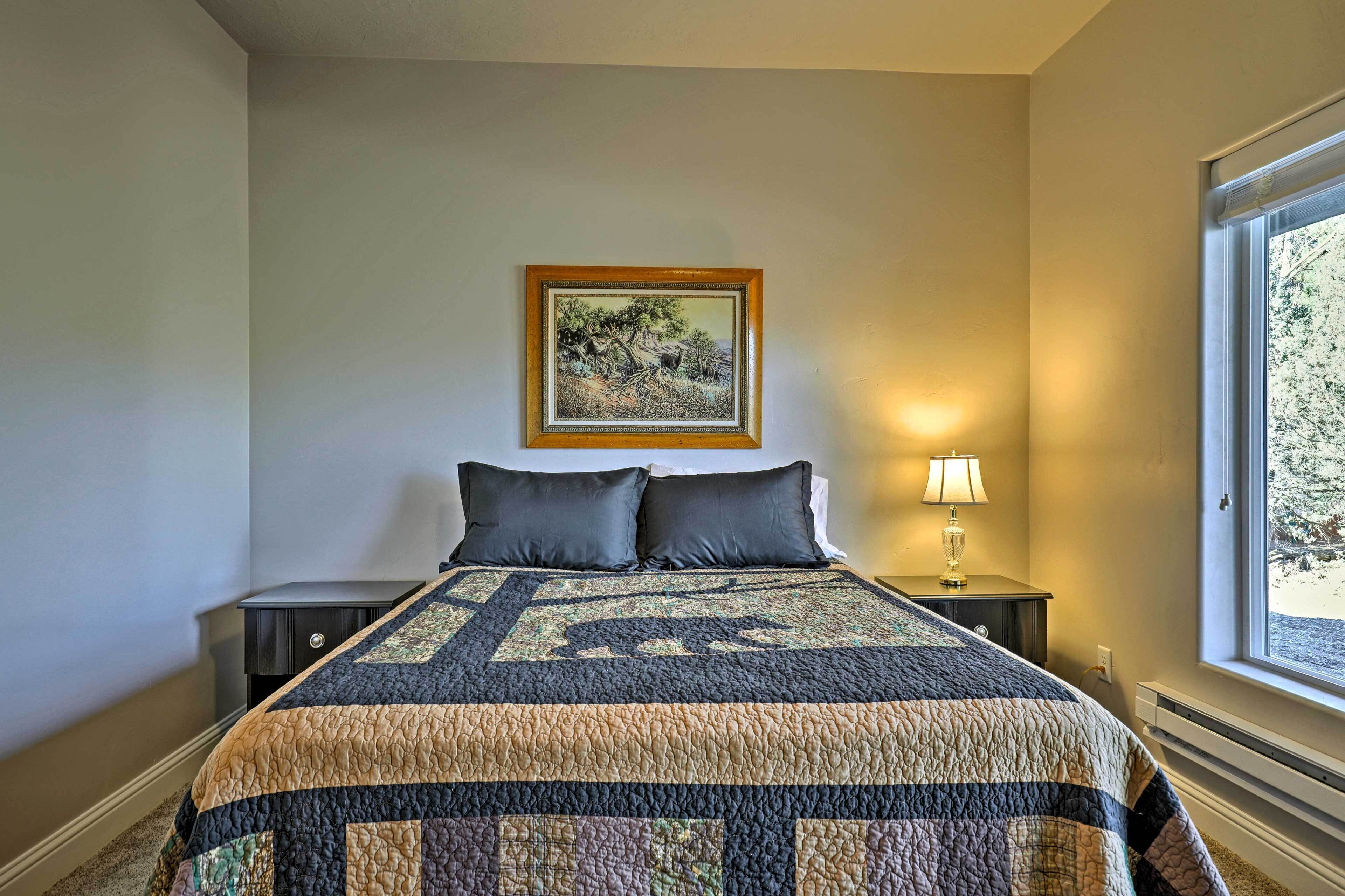 A bedroom with a large bed, a nightstand with a lamp, a framed picture on the wall, and a window.