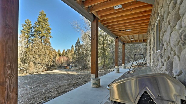 A covered outdoor area with a stone wall and wooden beams, a concrete floor, and a metal grill. - Mammoth Creek Apt. Between Bryce Canyon & Zion! (Hatch)