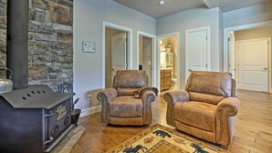 A living room with two leather recliners, a stone wall, a wood-burning stove, and a patterned rug. - Mammoth Creek Apt. Between Bryce Canyon & Zion! (Hatch)