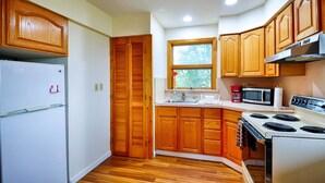 Une cuisine compacte avec des meubles en bois, un réfrigérateur blanc, un four à micro-ondes, une cuisinière et une fenêtre qui laisse entrer la lumière naturelle.