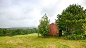 Une grange rouge, située dans un cadre rural, avec un champ herbeux et des arbres en arrière-plan.