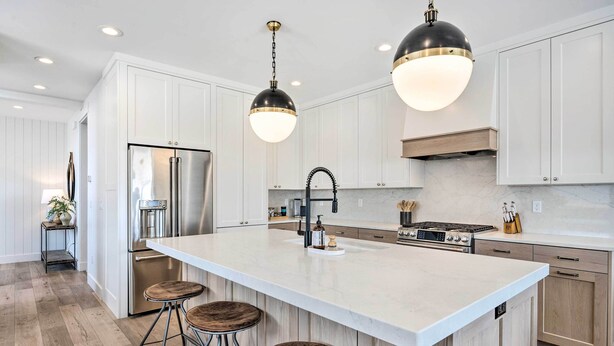 A modern kitchen with white cabinetry, stainless steel appliances, a large island with stools, pendant lighting, and a marble backsplash. - Mountain-view Townhome Near Powder Mountain! (Huntsville)