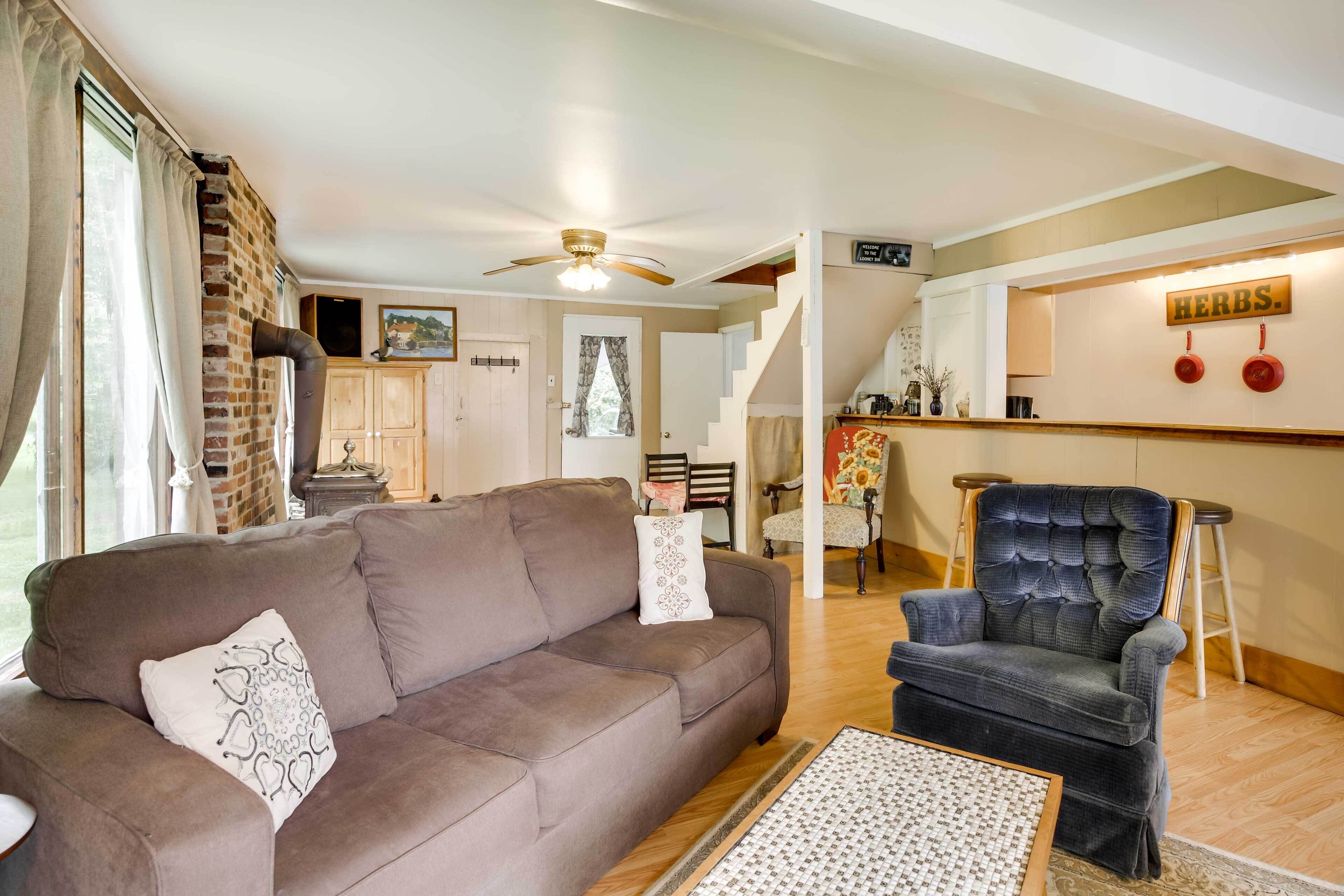 A living room with a brown sofa, a patterned coffee table, and a blue armchair. There is a brick wall and a ceiling fan.
