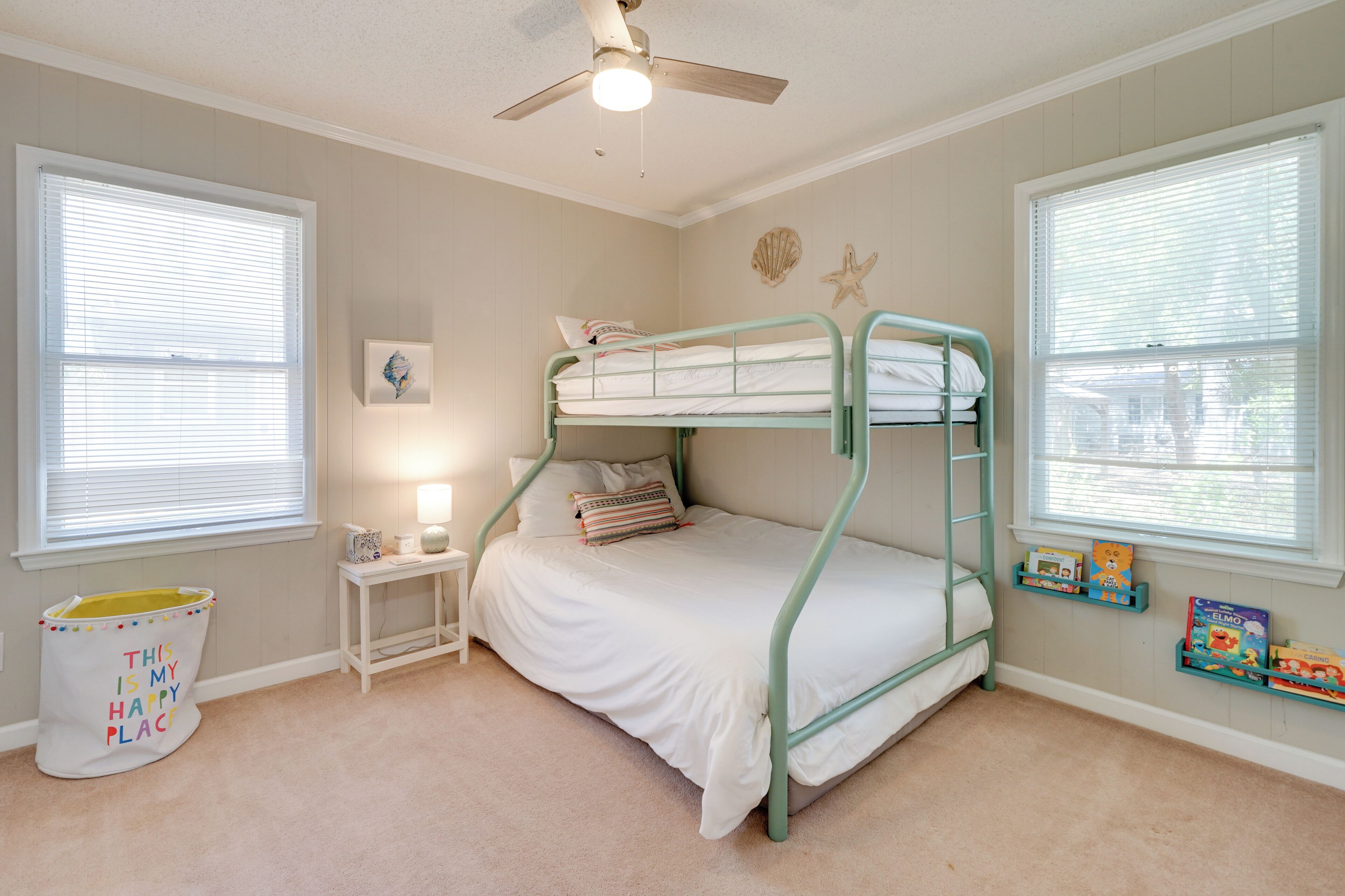 Une chambre avec un lit superposé, un ventilateur de plafond, une table de chevet, une lampe et une fenêtre avec des stores.