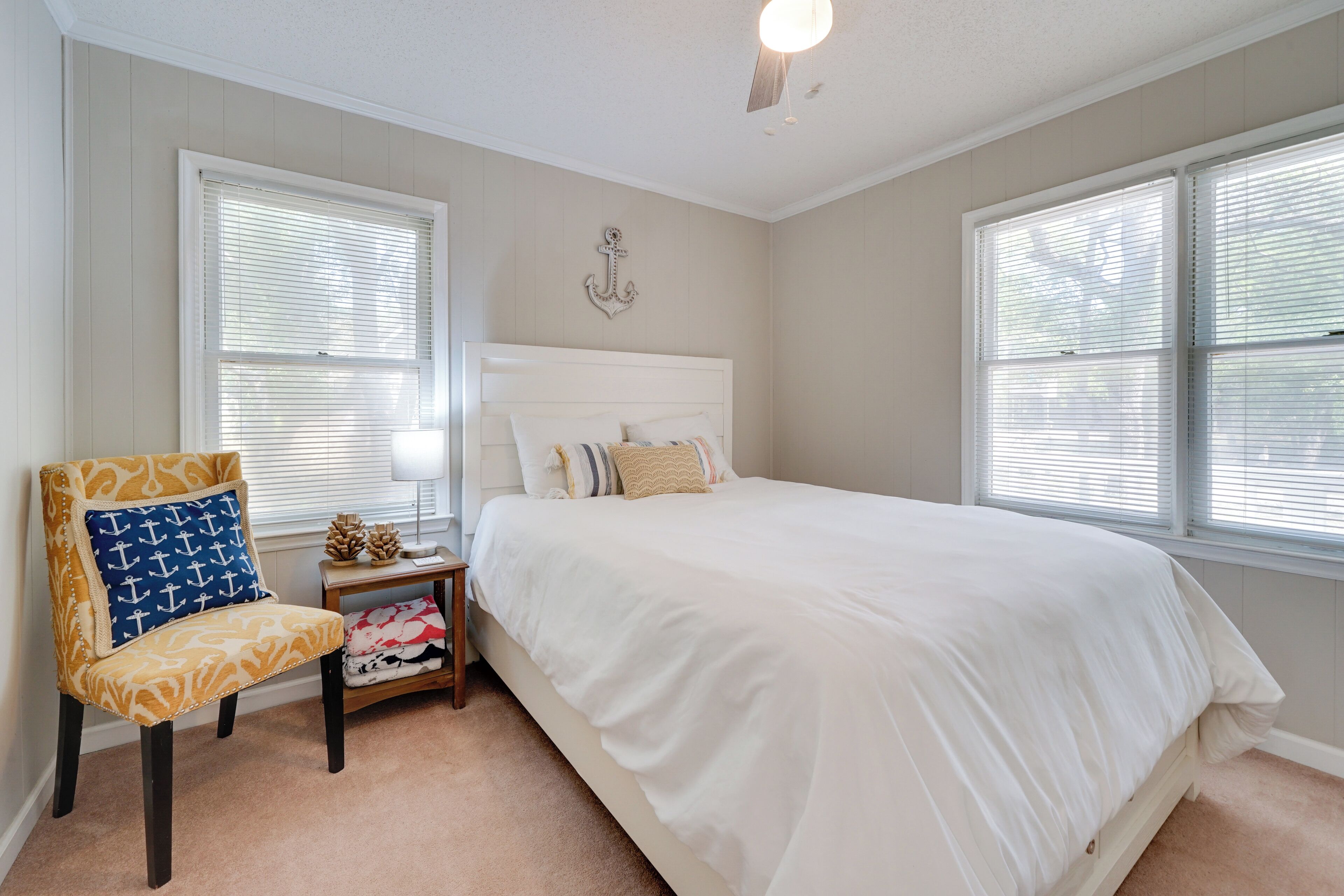 A bedroom with a large bed, a chair with a nautical pattern, and a small table with decorative items.
