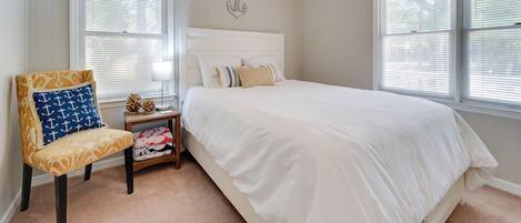 A bedroom with a large bed, a chair with a nautical pattern, and a small table with decorative items.