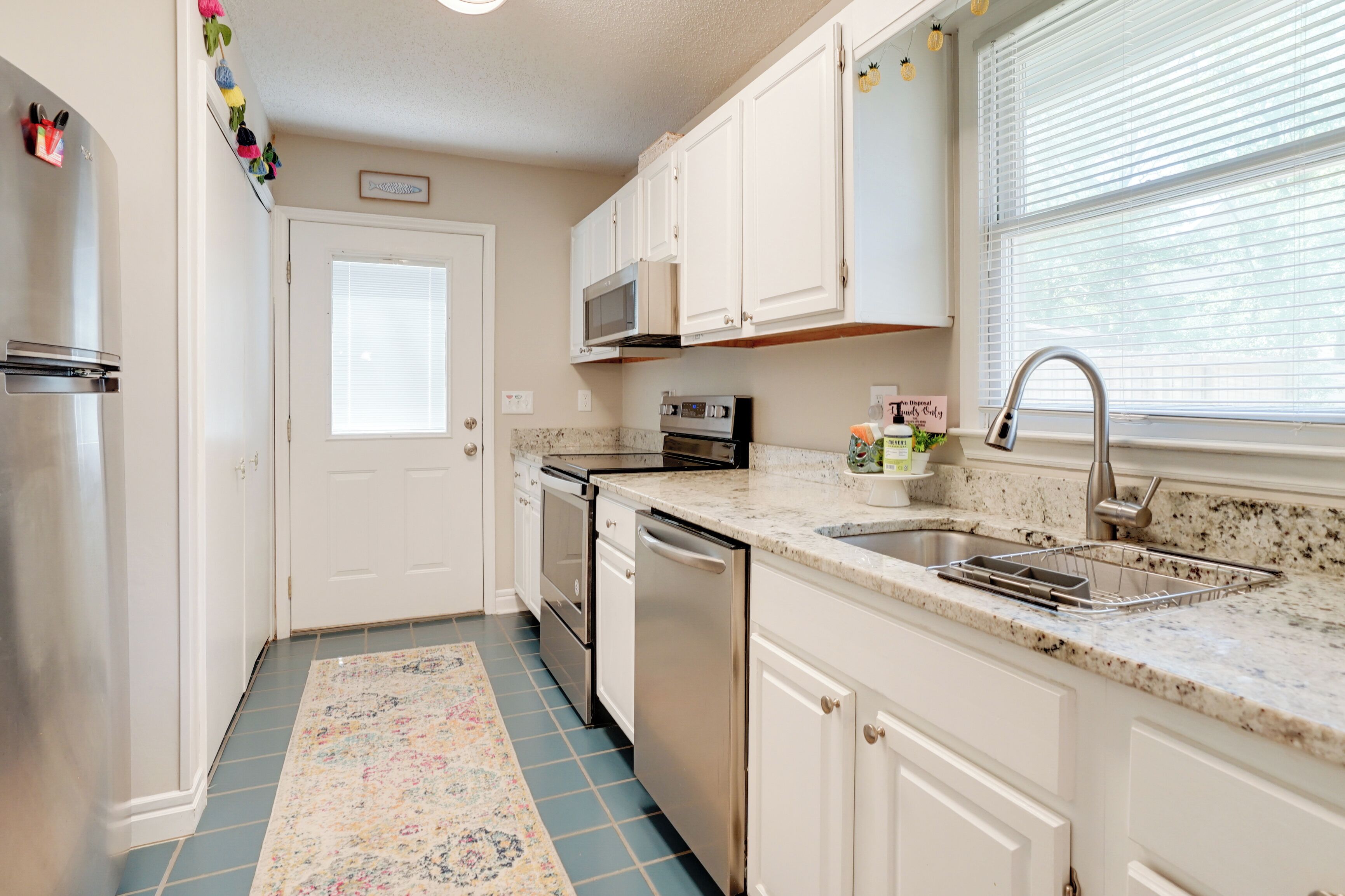 A kitchen with white cabinets, stainless steel appliances, a granite countertop, and a window with blinds.