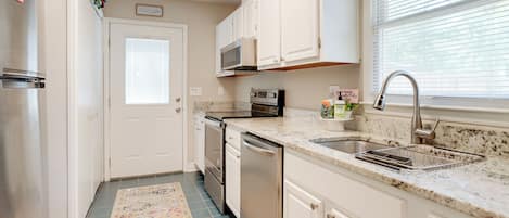 A kitchen with white cabinets, stainless steel appliances, a granite countertop, and a window with blinds.