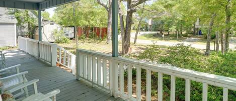 A covered porch with white railings, a ceiling fan, and a view of a residential area with trees and a fence.