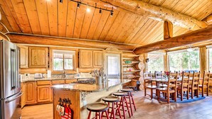 A spacious kitchen with wooden cabinets, a large island with stools, and a dining area with wooden chairs. - < 1 Mi to Lake Granby: Log Cabin w/ Fire Pit (Grand Lake)