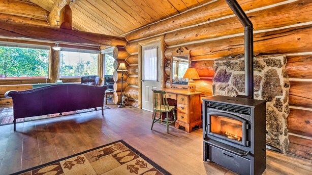 A log cabin interior with a stone fireplace, wooden walls, a purple sofa, and a wooden desk. - < 1 Mi to Lake Granby: Log Cabin w/ Fire Pit (Grand Lake)