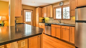 A kitchen with wooden cabinets, a stainless steel refrigerator, a dishwasher, and a window with a view of trees. - Mountaintop Ellicottville Home: 7 Mi to Ski Resort (Ellicottville)