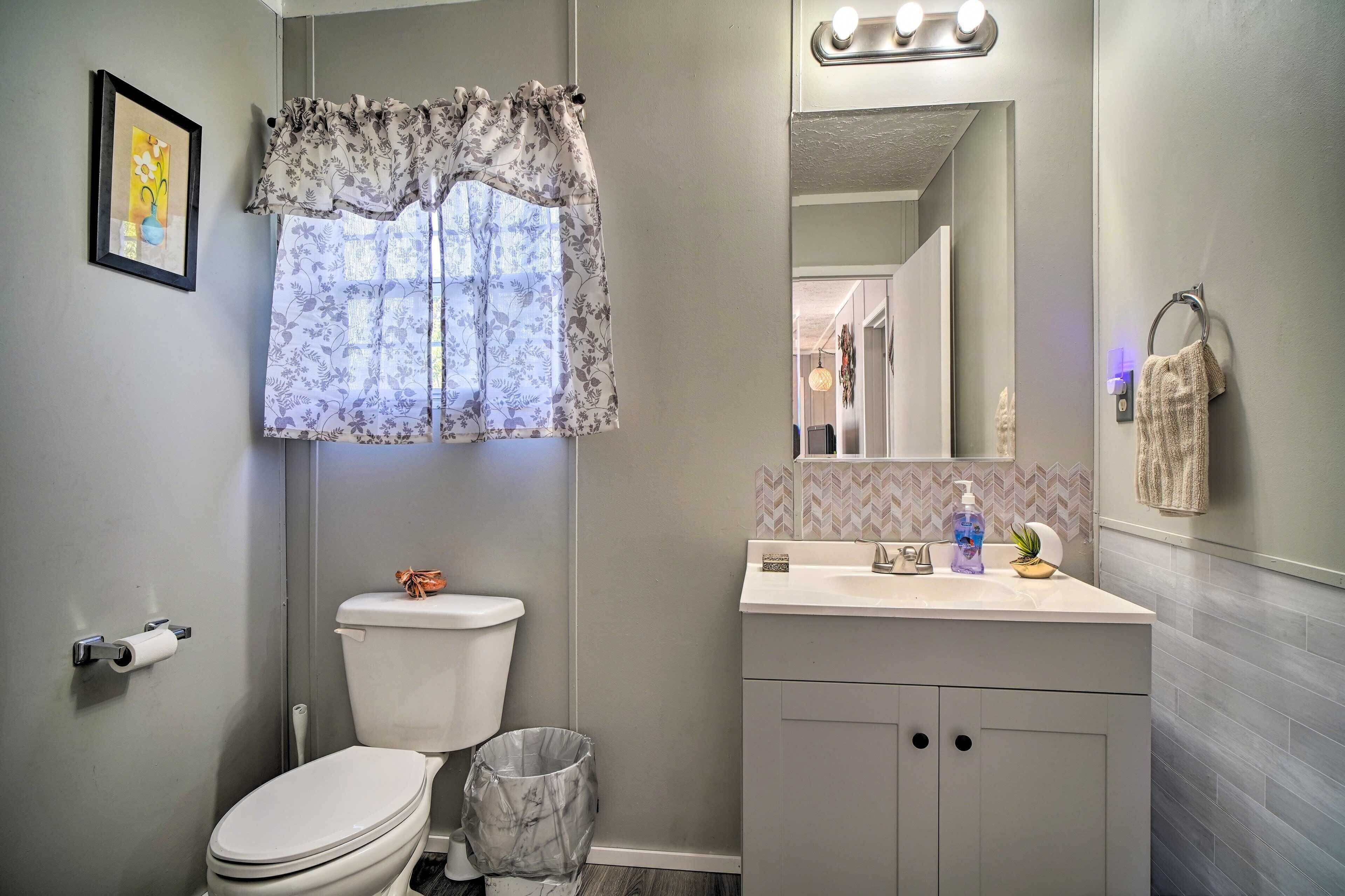A bathroom with a toilet, a sink with a mirror, and a trash can.