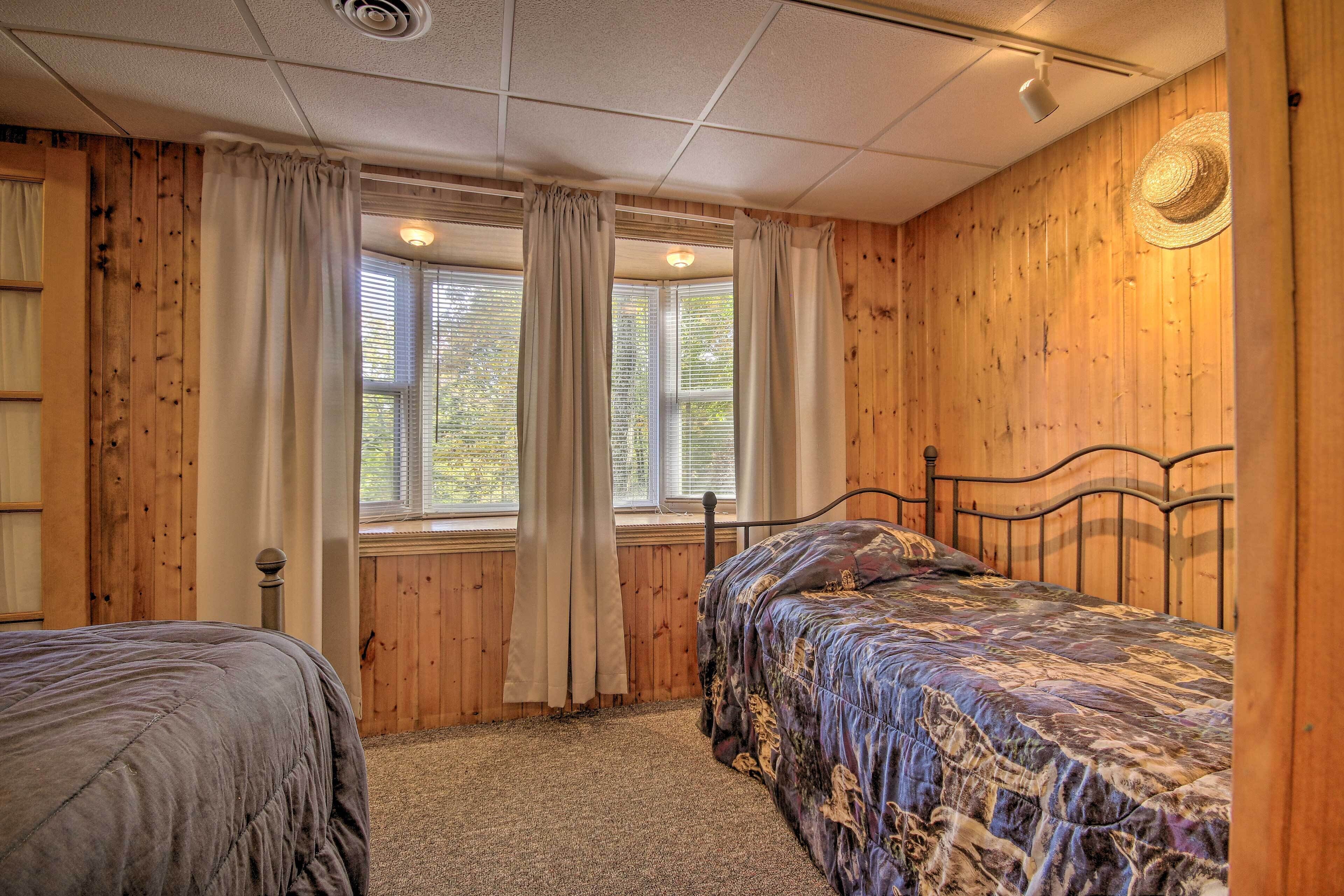 A bedroom with two beds, wooden walls, a large window with curtains, and a ceiling light.