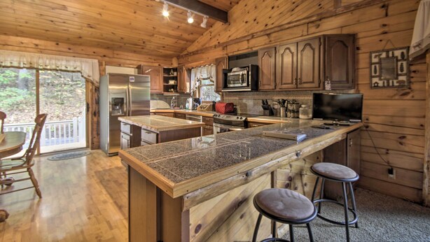 Cocina de cabaña de madera con una isla grande, taburetes de bar, un refrigerador, un microondas y una estufa.
