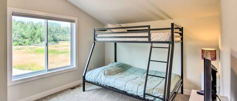 Una cama en literas en una habitación con un ventanal grande, un escritorio y una lámpara.