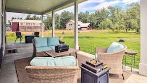 Een overdekt terras met rieten meubilair, een barbecue en uitzicht op een schuur en huis in een landelijke omgeving.