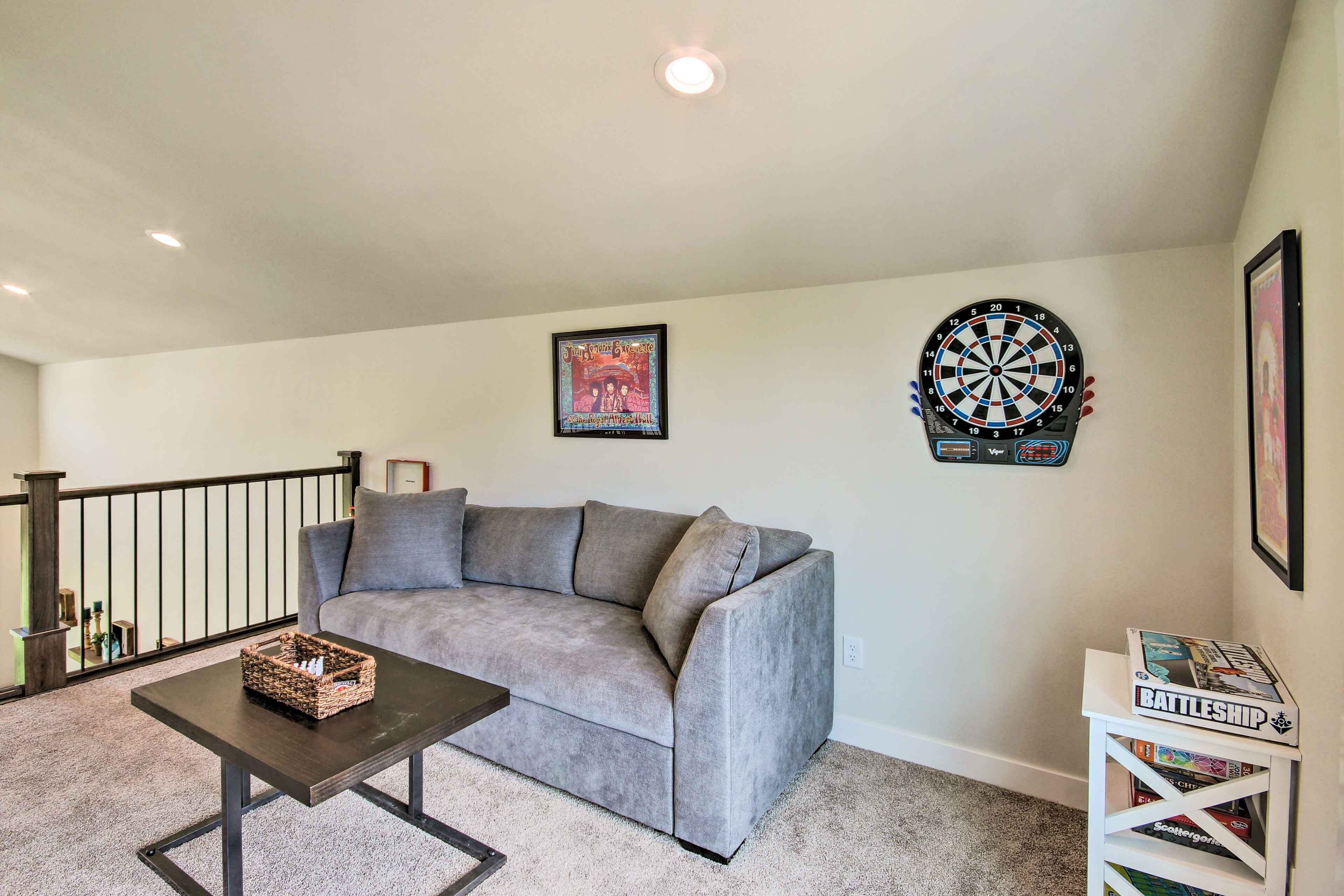 A living room with a gray sofa, a coffee table, a dartboard, and a bookshelf.