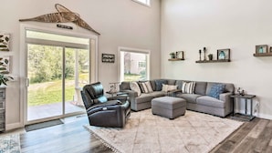 Een ruime woonkamer met een hoekbank, een lederen fauteuil en een groot raam.