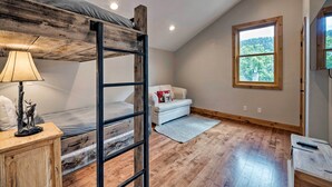 A bedroom with a bunk bed, a small sofa, a window with a view of trees, and a lamp on a wooden cabinet. - Quiet Park City Home w/ Hot Tub - Walk to Main St! (Park City)